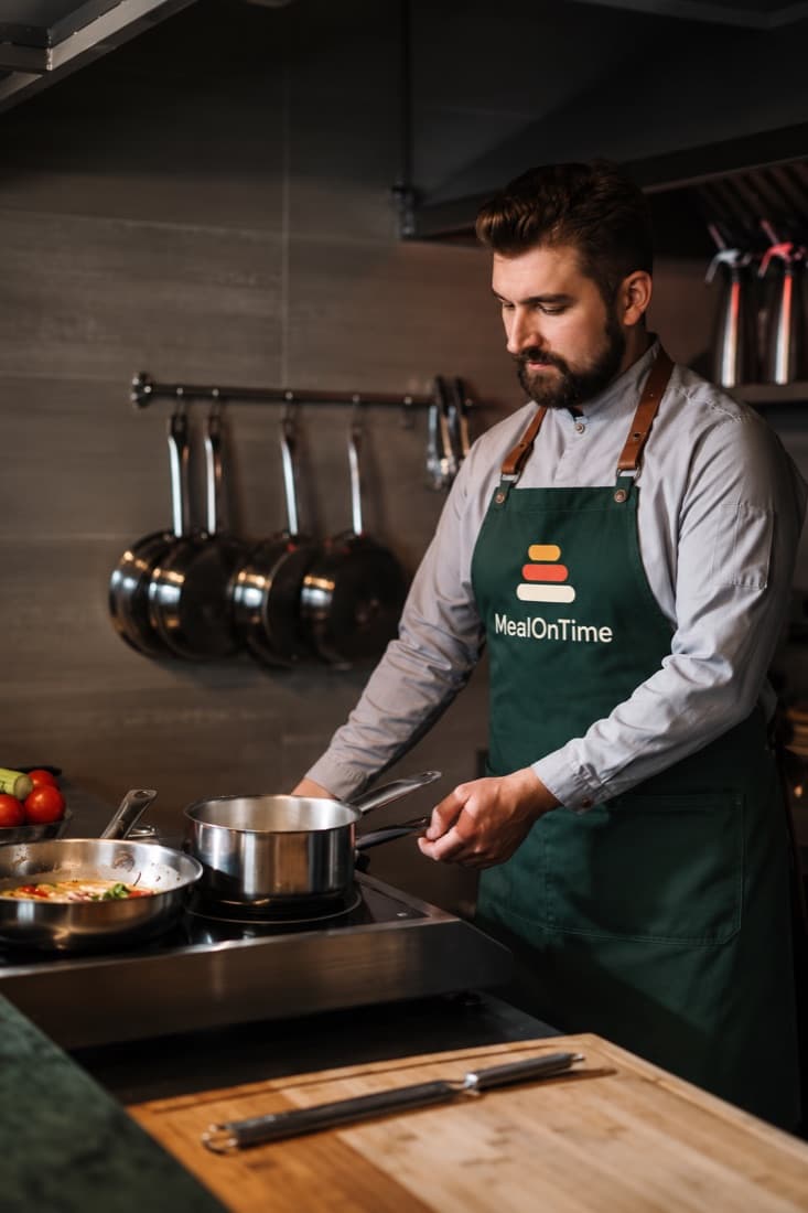 Un cuisinier en tablier MealOnTime devant ses casseroles